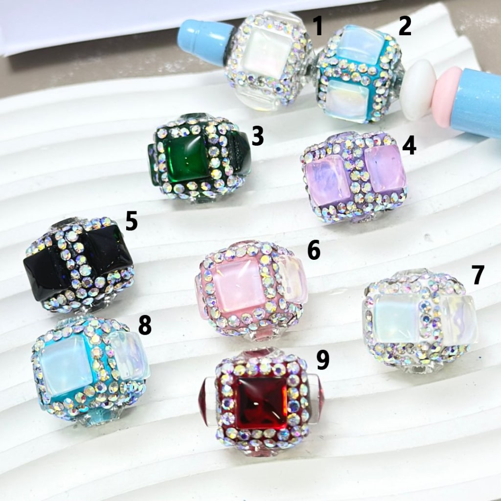 A collection of square cube clay beads, each embellished with clear and colored rhinestones.
