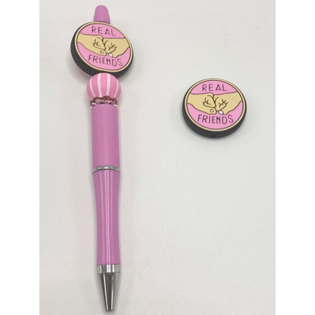 A silicone bead with the phrase 'REAL FRIENDS' in the center, featuring a design with hands and pink background.