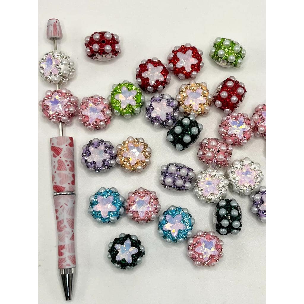 A collection of multicolored clay beads with flatback pearls and fancy star rhinestones. They are displayed alongside a pen for scale.