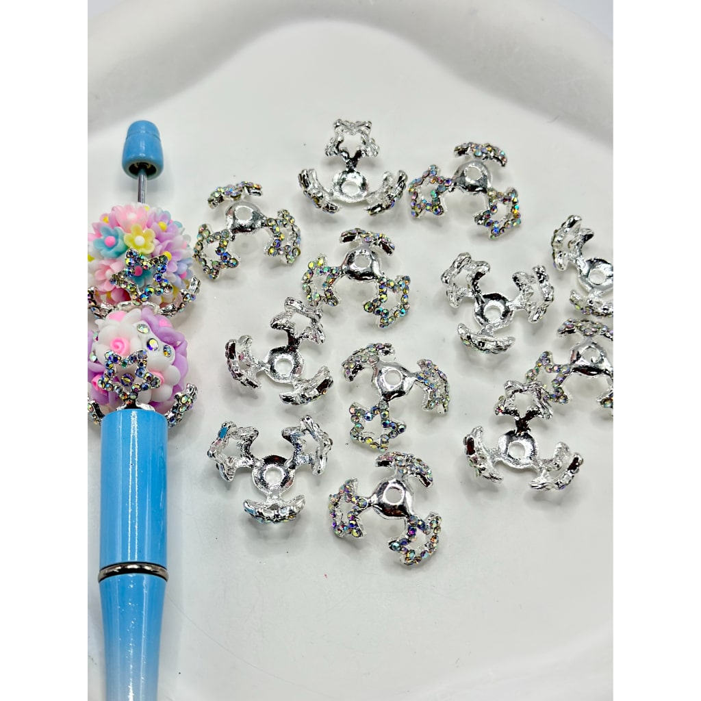 A collection of silver-colored beads with AB rhinestones cage bead caps displayed alongside a blue stylus pen with a multicolor bead on its tip.