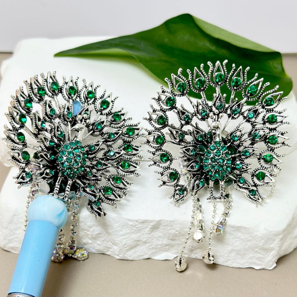 Two silver alloy brooches featuring a peacock design with green mini rhinestones, white pearls, and other embellishments such as heart shapes and chains.