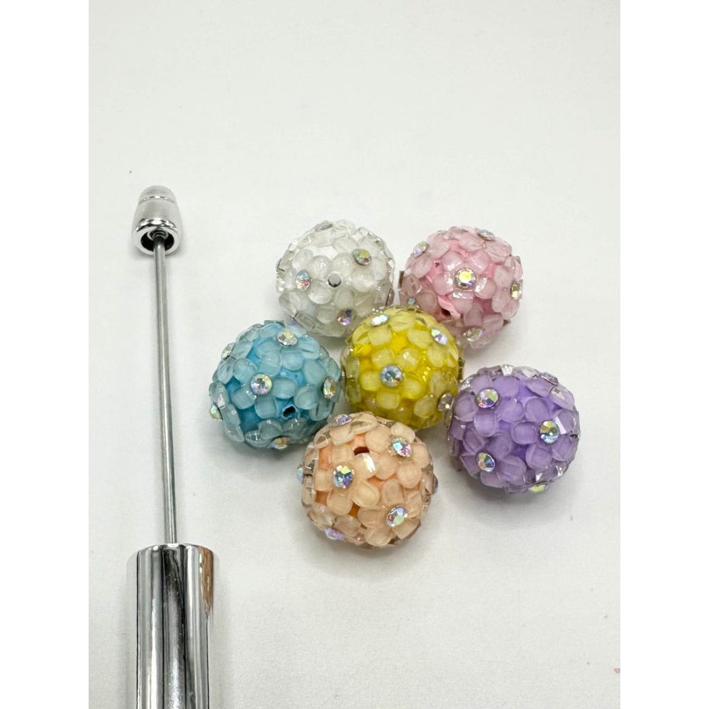 A collection of multicolored floral clay beads with rhinestone flowers, displayed alongside a pick-up tool.