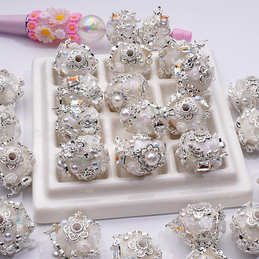 Decorative silver and pearl beads on a white tray with a pink hairbrush in the background.