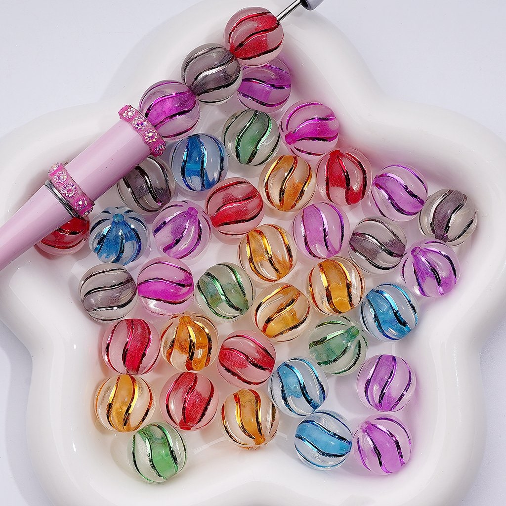 Colorful glass beads on a white surface with a pink tool.

