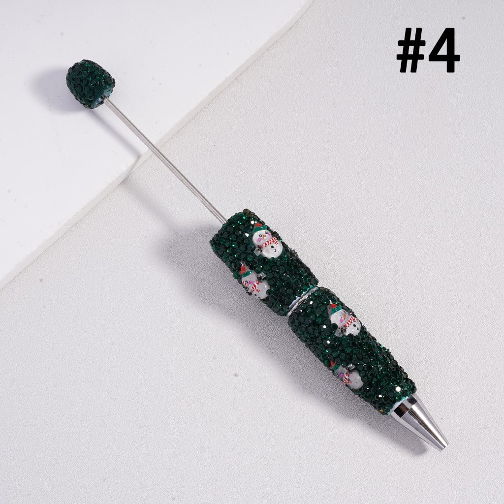 Decorative pen with green bead design and small snowman figures on a white background


