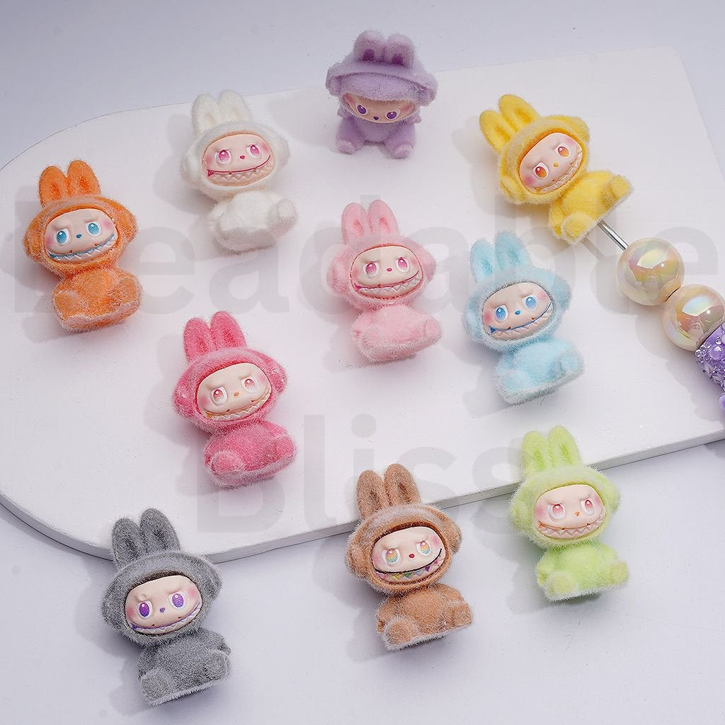 Colorful cartoon character earrings on a white surface with a brand name visible.


