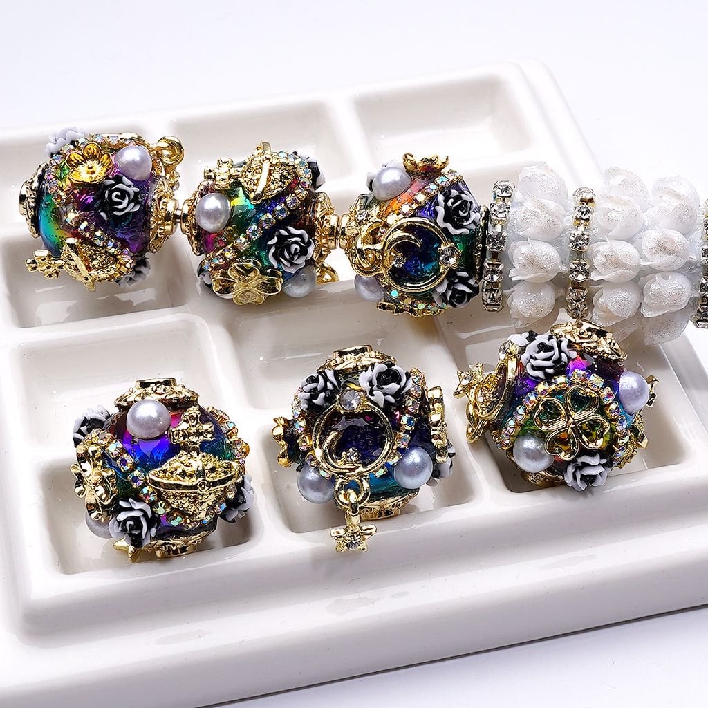 Decorative beads with intricate designs and pearls on a white tray.

