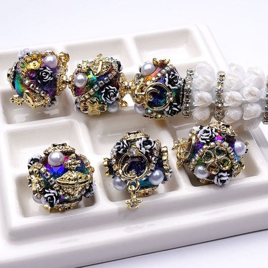 Decorative beads with intricate designs and pearls on a white tray.

