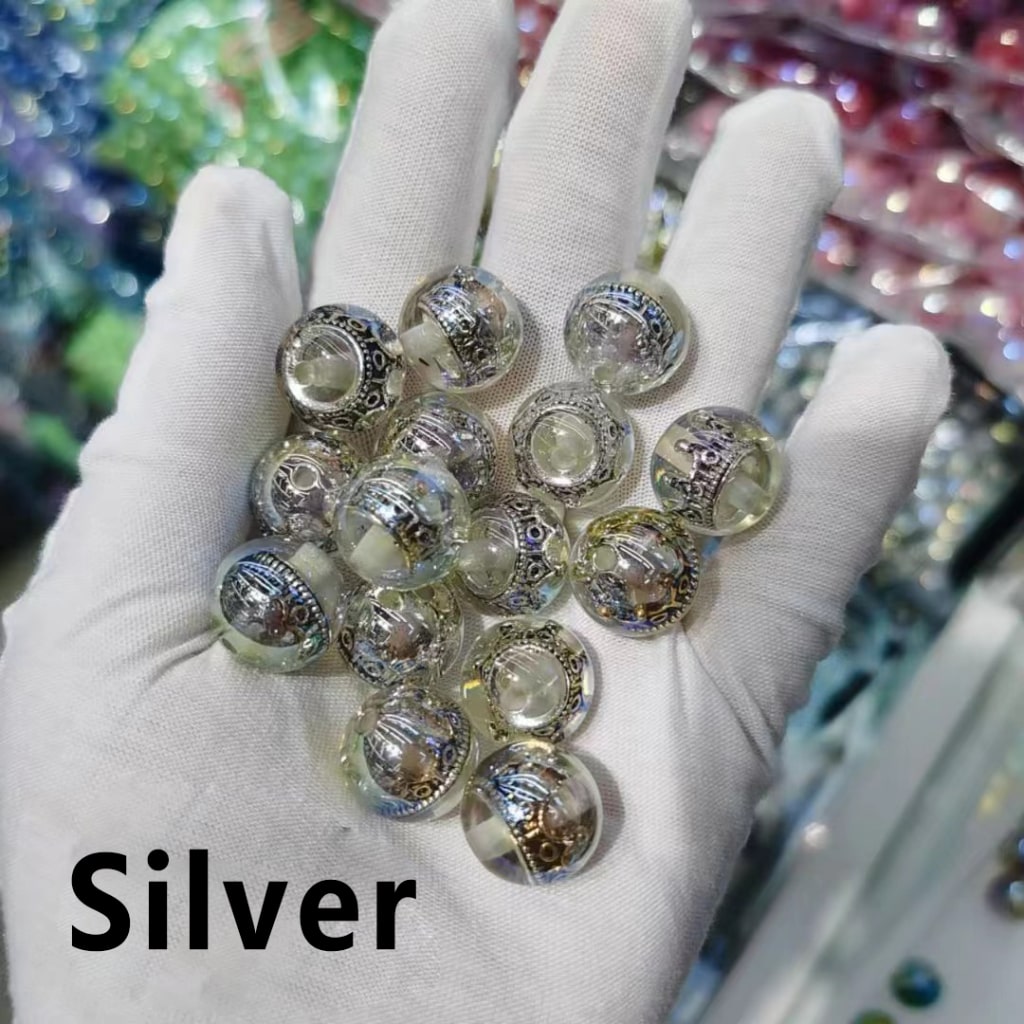 Hand wearing a white glove holding silver beads with a blurred colorful background

