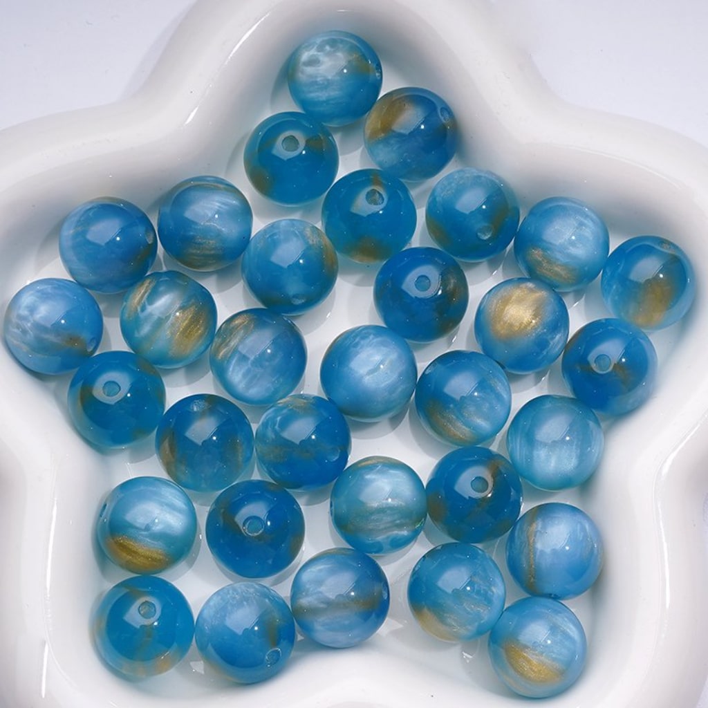 A selection of colorful round acrylic beads in various colors displayed alongside a pen with a bead attached to its cap.

