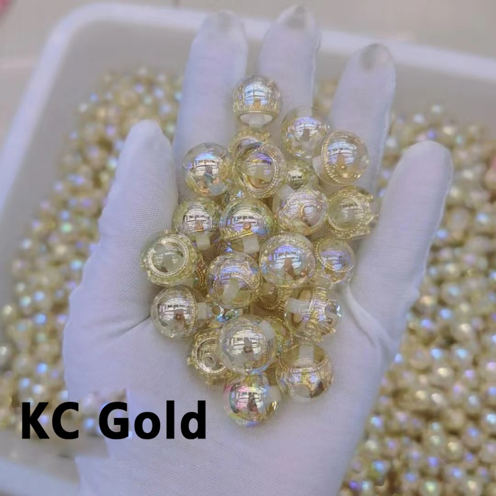 Hand holding gold beads with 'KC Gold' text on a white background

