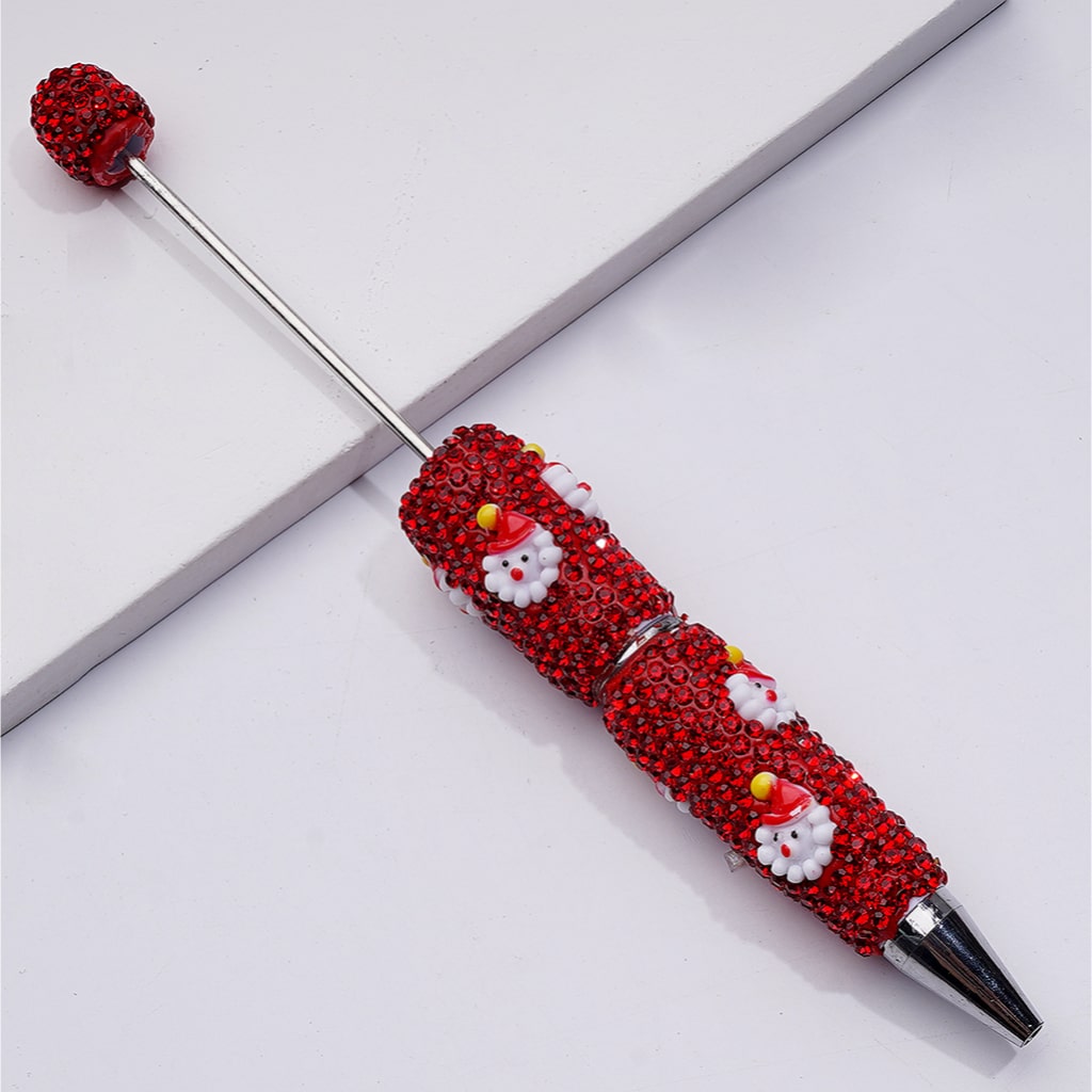 Decorative pen with red gemstones and Santa Claus figures on a white background

