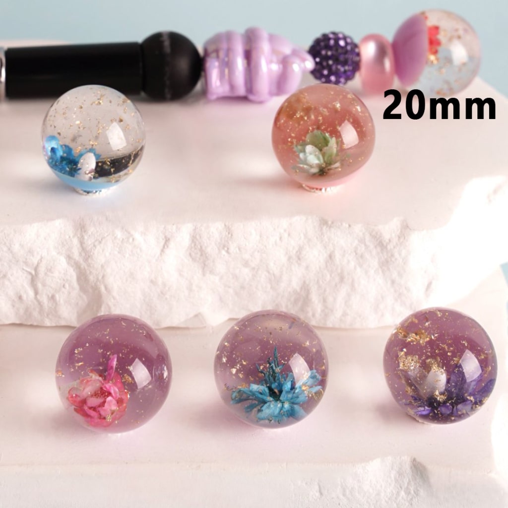 A collection of clear round acrylic beads with gold foil flakes and cute flowers inside, displayed on a white surface. The beads are 20mm in size and come in a variety of colors.

