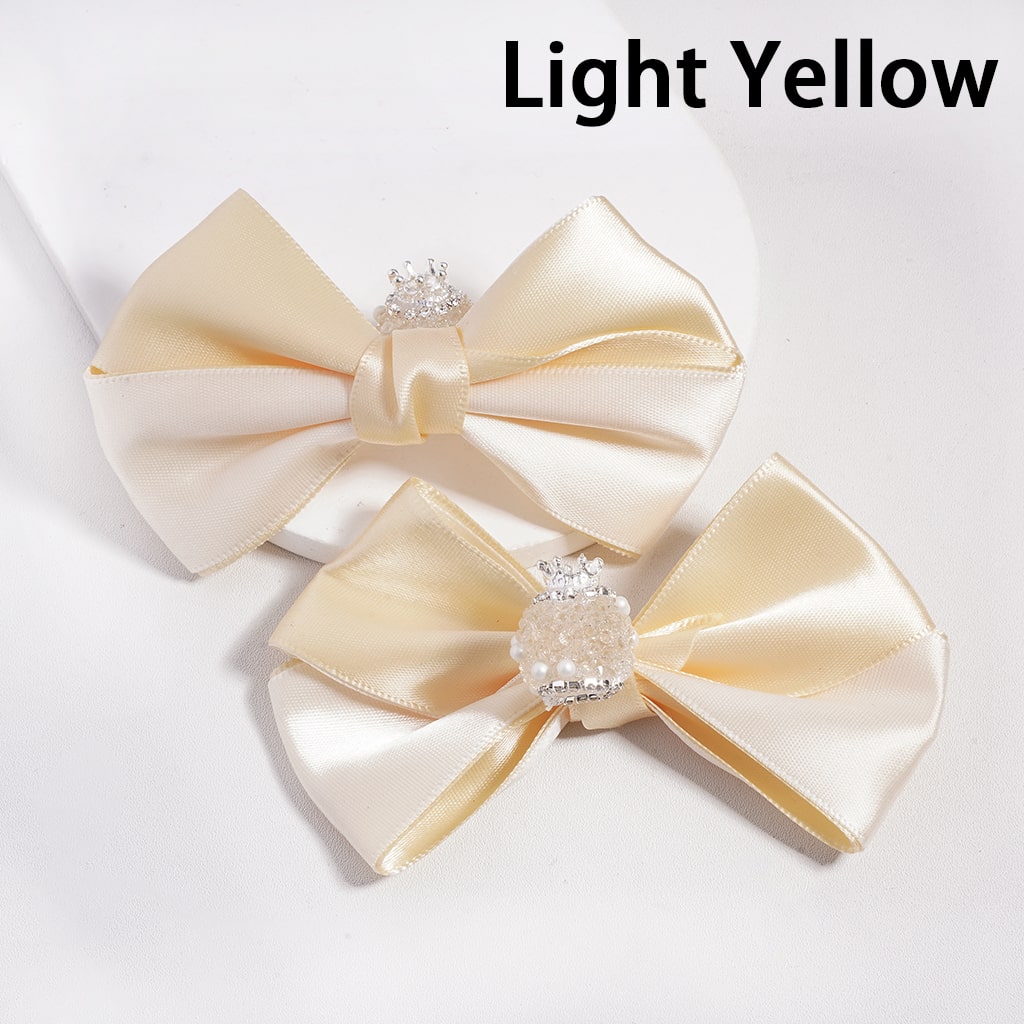 Two light yellow satin bows with decorative centers on a white background.

