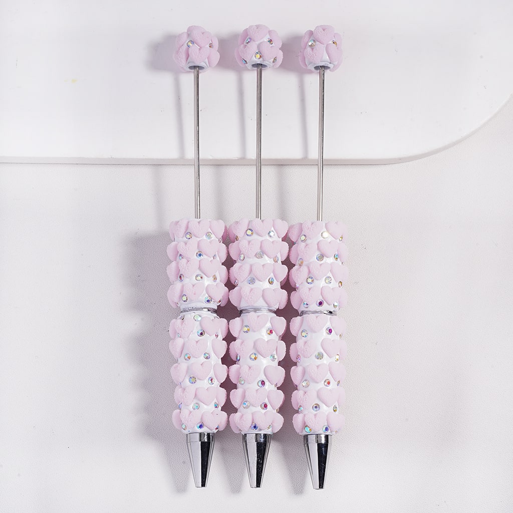 Three decorative pens with pink floral designs and rhinestones on a white background