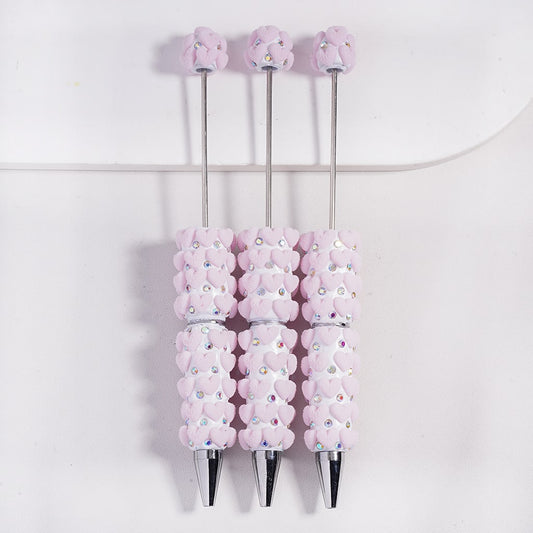 Three decorative pens with pink floral designs and rhinestones on a white background