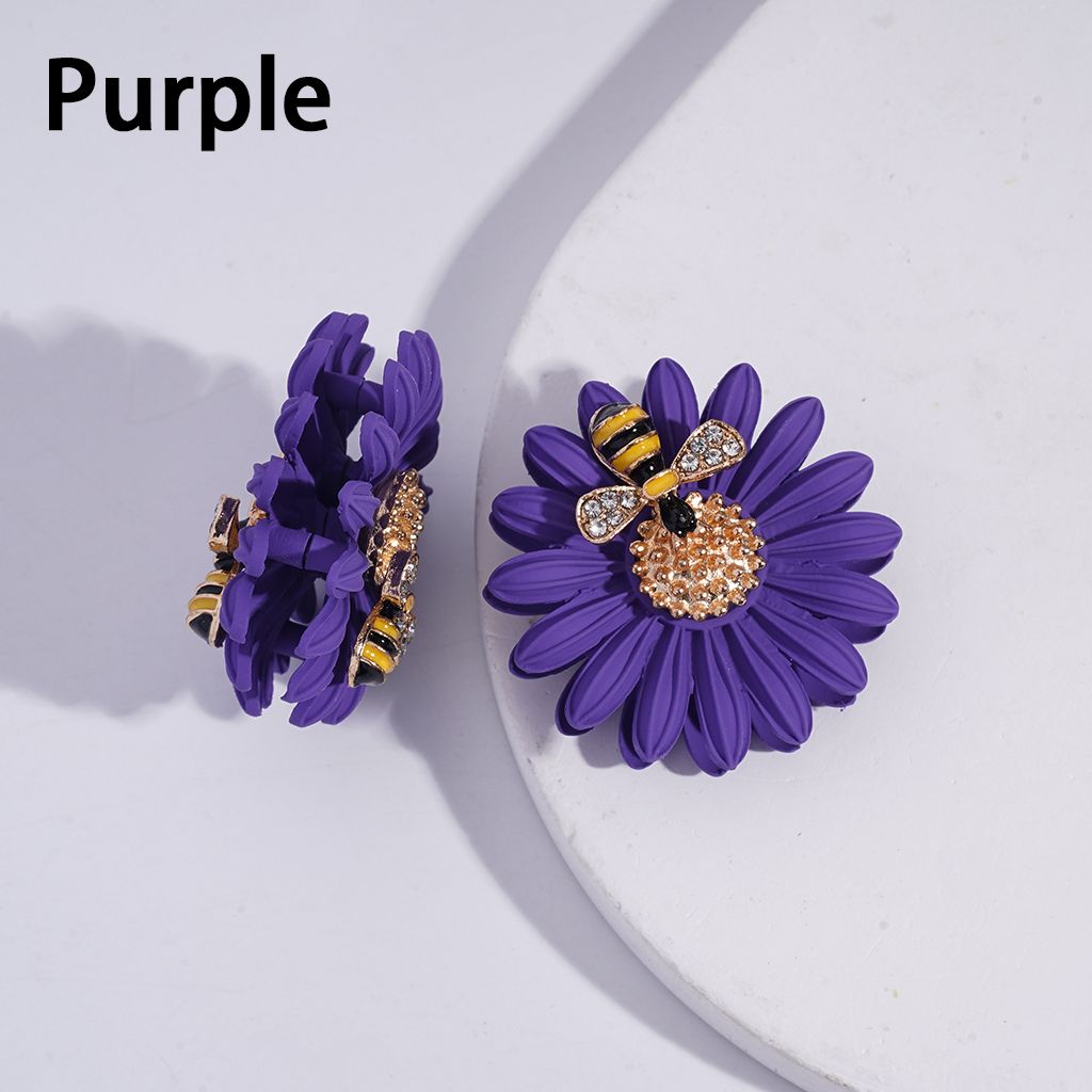 Purple flower-shaped earrings with bee accents on a white background