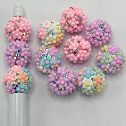 A collection of multicolored round clay beads with floral patterns and rhinestone embellishments.

