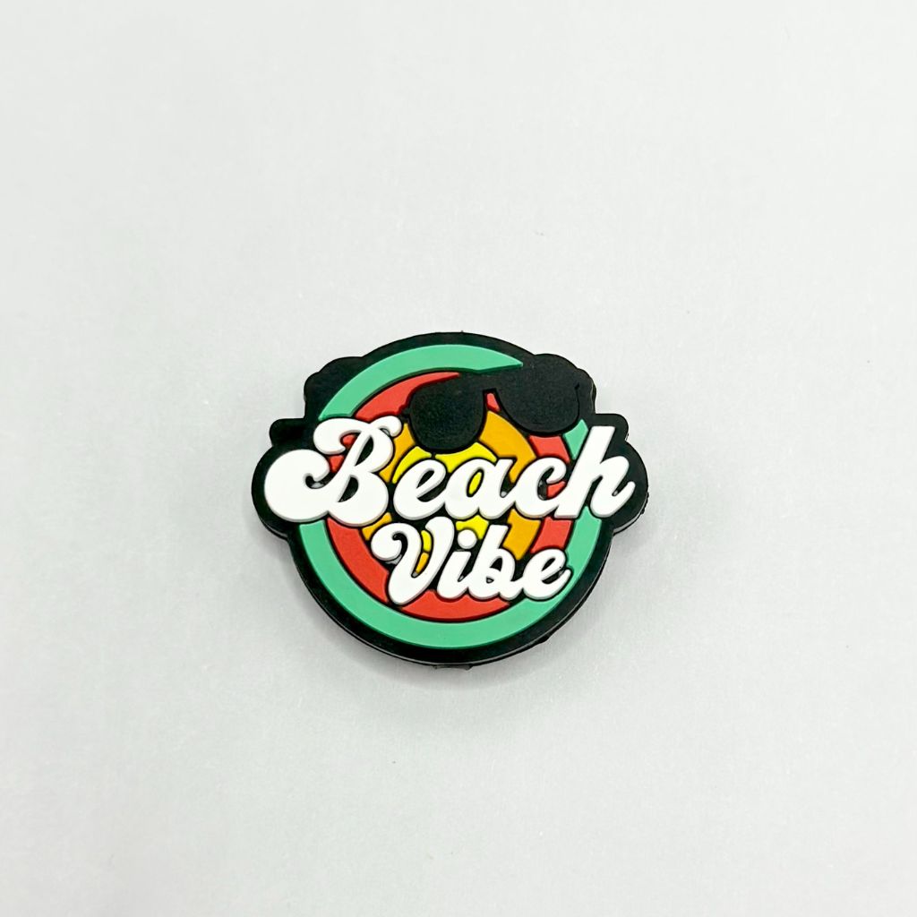 A silicone bead with a beach vibe text and beach colors, circular in shape, with a hole in the center for stringing purposes.


