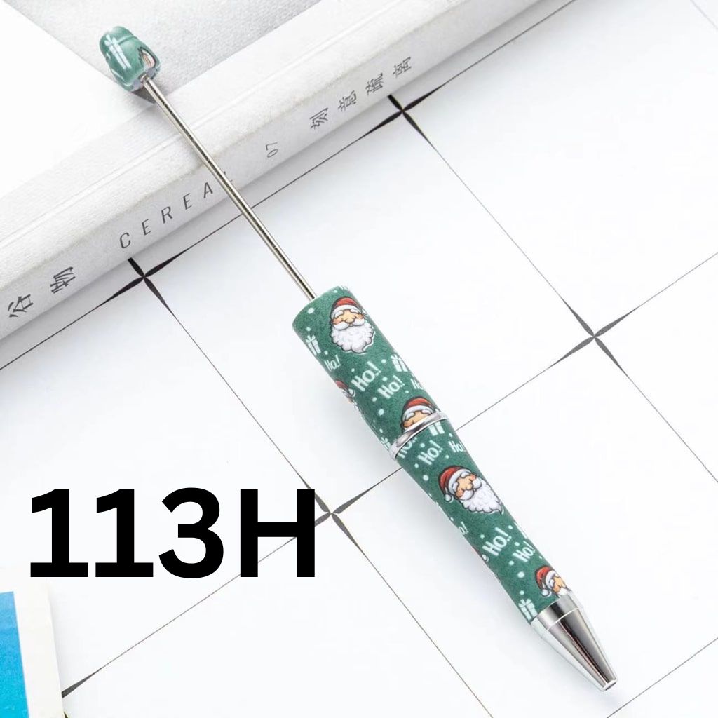 A green beadable pen with floral patterns and a cartoon character design, lying on a tiled surface with a ruler for scale.

