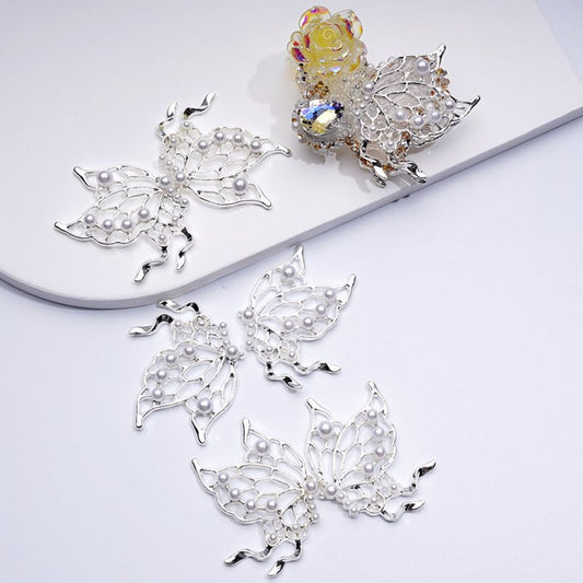 A collection of butterfly-shaped silver alloy beads with white pearls, displayed on a white surface.

