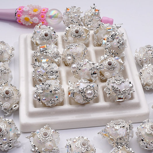 Decorative silver and pearl beads on a white tray with a pink hairbrush in the background.

