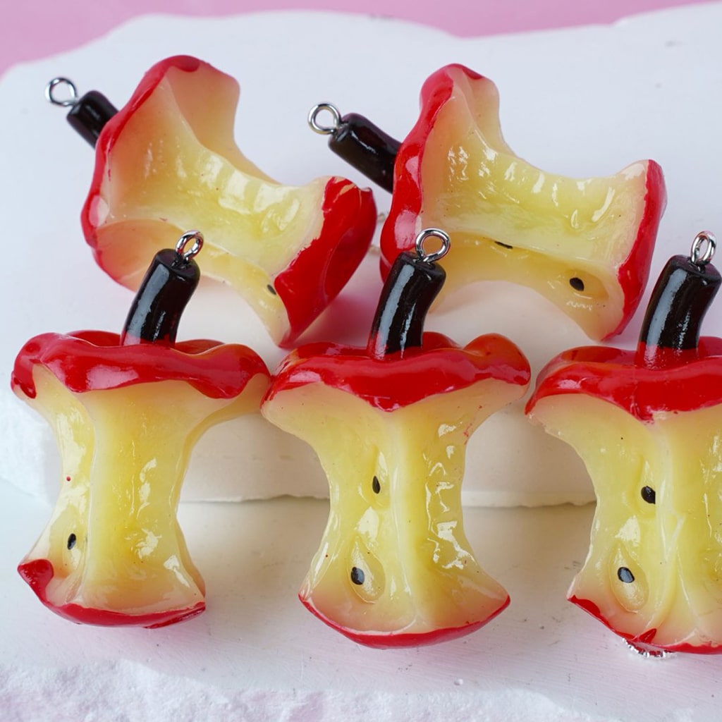 A collection of apple core-shaped pendant accessories with red and yellow colors and black wires attached to them.

