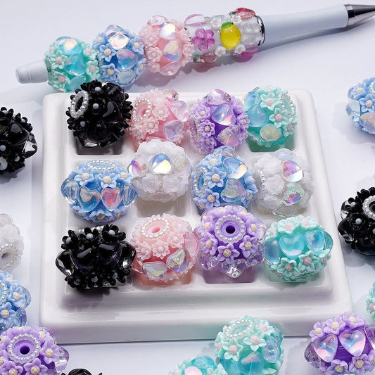 Assorted colorful decorative beads on a white tray with a pen in the background.

