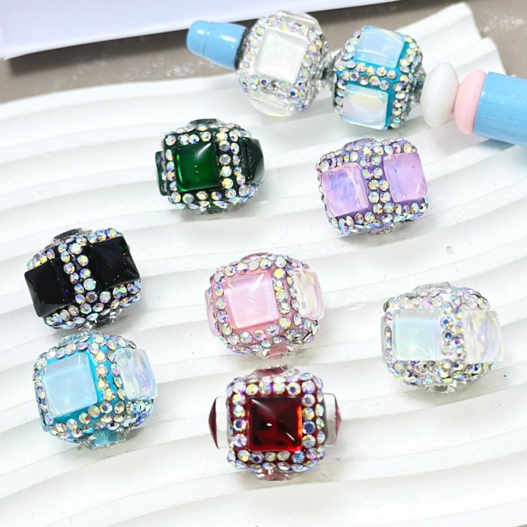 A collection of square cube clay beads, each embellished with clear and colored rhinestones.

