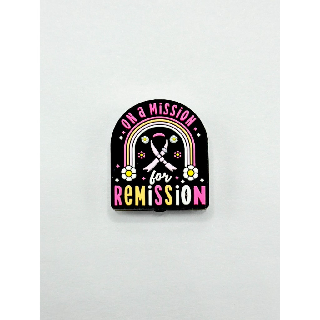 A silicone bead with the text 'Fight with Cancer On a Mission Remission' printed on it, featuring a black background with pink and yellow accents and a cross symbol.

