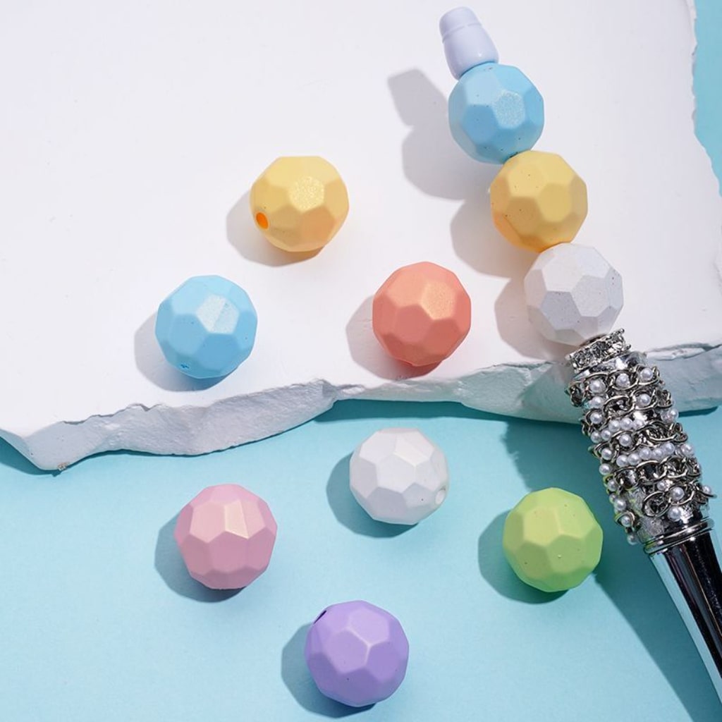 Pastel-colored geometric beads on a light blue surface with a decorative pen.

