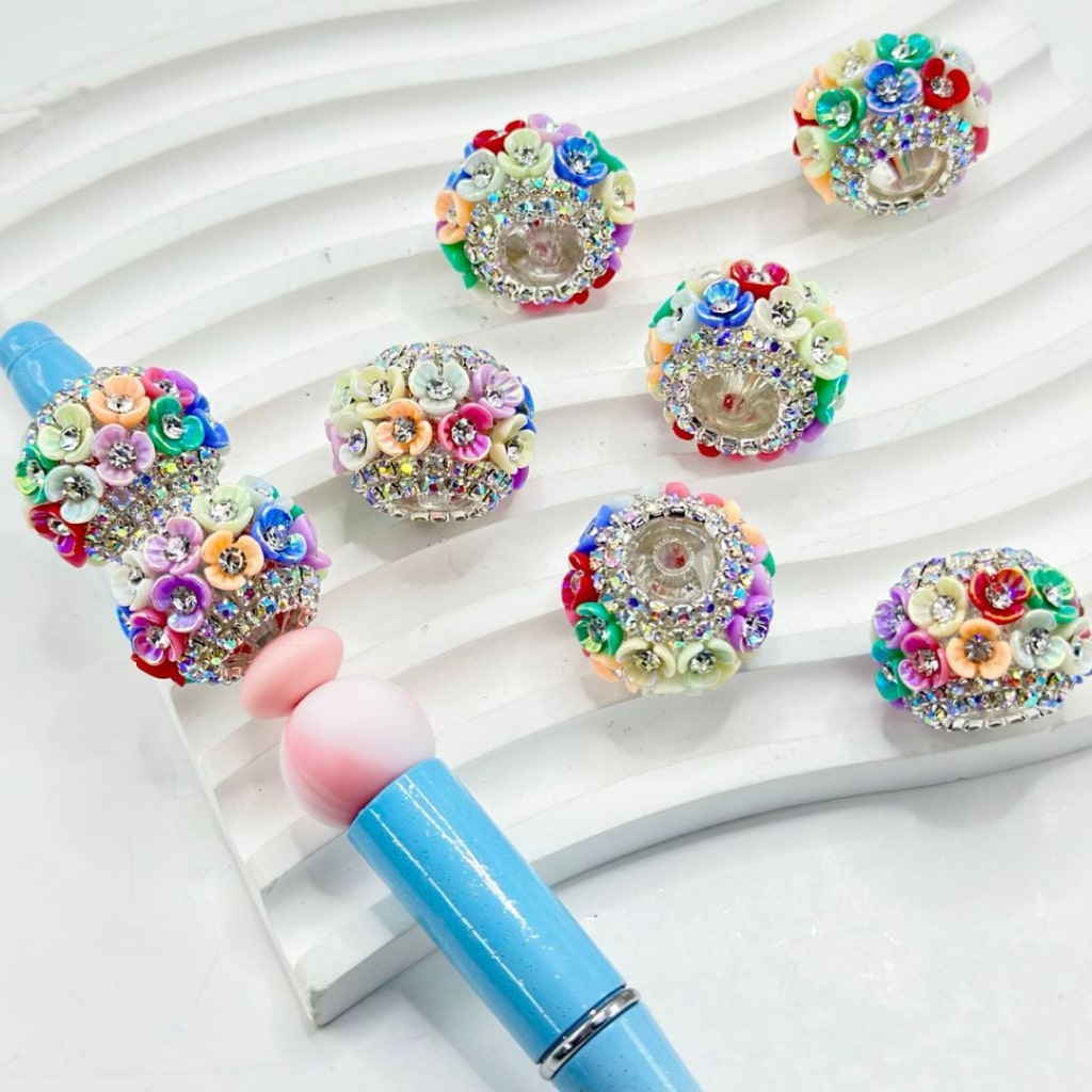 Clear acrylic beads with multicolored rhinestones inside, arranged around a pen to form a floral pattern.

