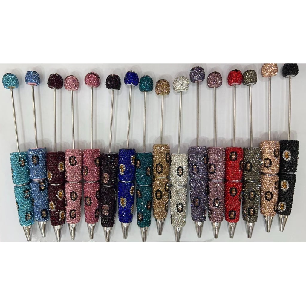 A collection of pens each with a decorative top covered in multicolored rhinestones, displayed in a row.

