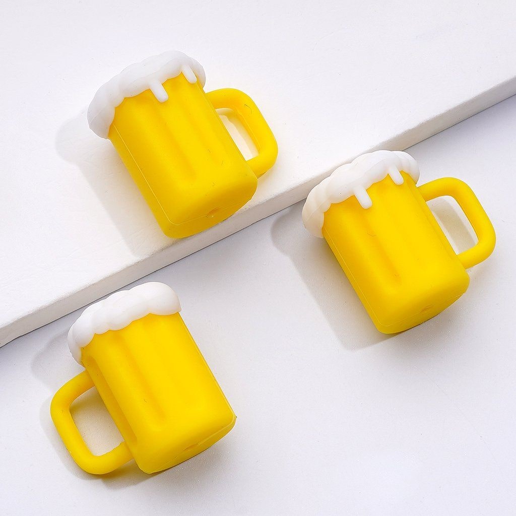 The image shows several silicone beads crafted to look like yellow beer bottles with white foam on top, mimicking the appearance of beer.

